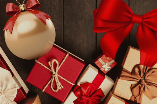 Gift boxes with red and brown ribbons and a gold ornament with a red bow on a wooden surface.