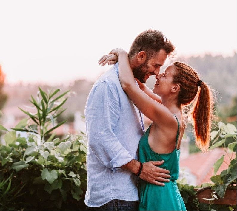 Couple embracing closely outdoors at sunset, sharing a joyful and intimate moment surrounded by greenery.