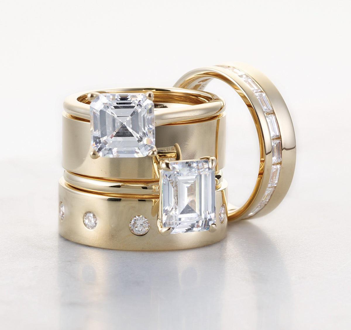 Stacked gold rings featuring two large emerald-cut diamonds and additional smaller diamonds set into polished bands, highlighting custom engagement ring design and craftsmanship.