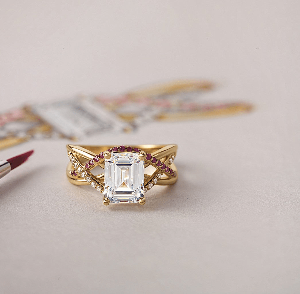 Emerald-cut diamond ring with intertwined gold bands accented by small rubies and diamonds on a soft surface.