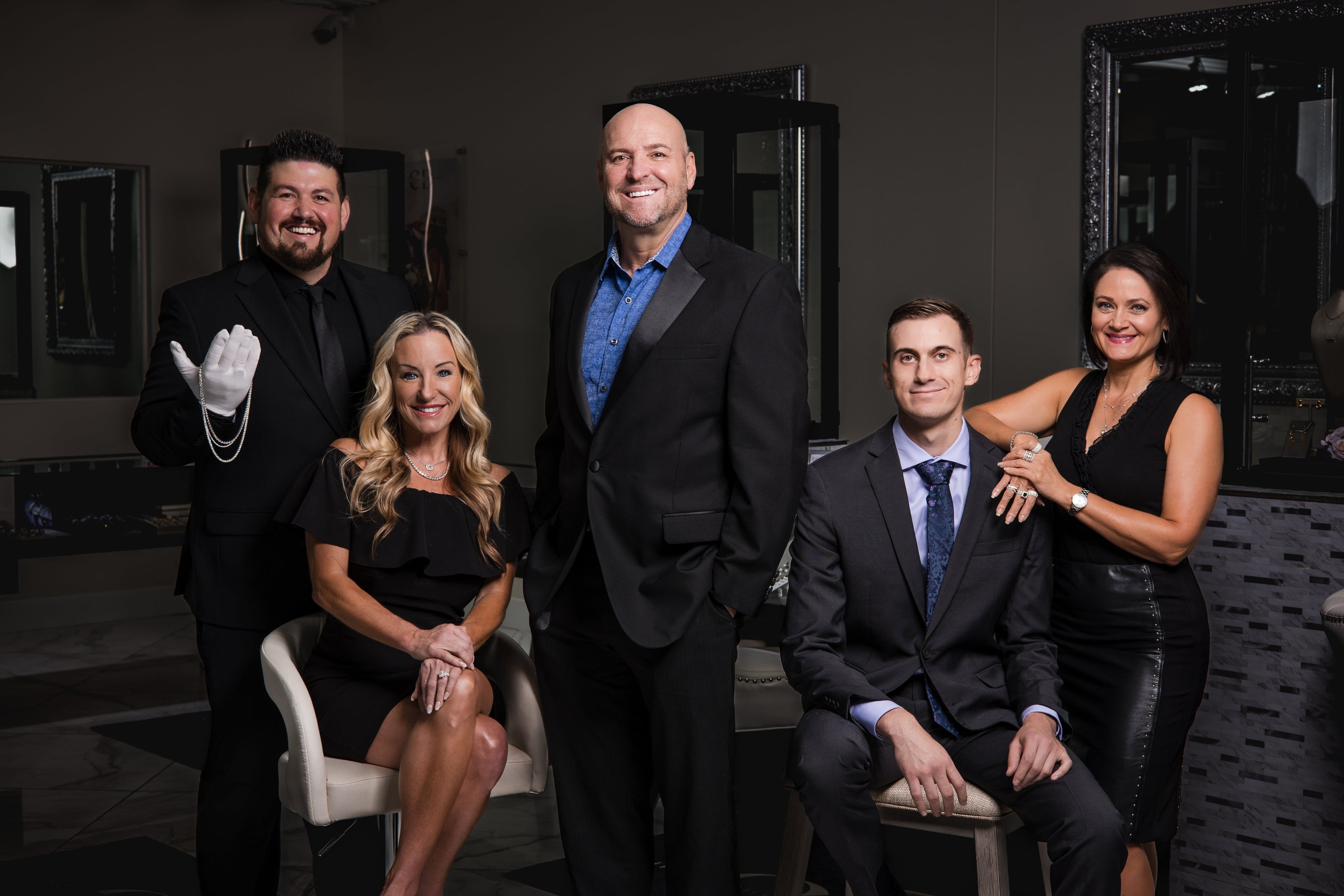 Five professionally dressed adults pose and smile in a modern, elegant room with dark decor and mirrors.