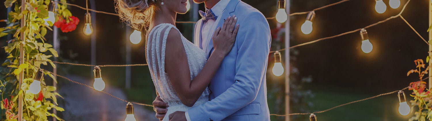 Bride and groom embracing under string lights at an outdoor wedding.