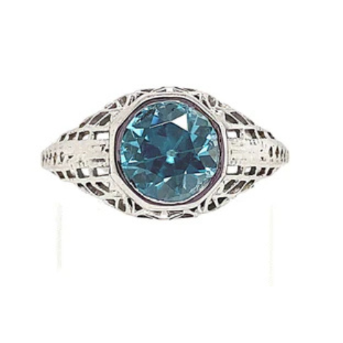 This vintage estate ring captures elegance perfectly, crafted in 14-karat white gold and highlighting a mesmerizing 7 mm round European cut blue zircon at its center, surrounded by intricate silver filigree work.