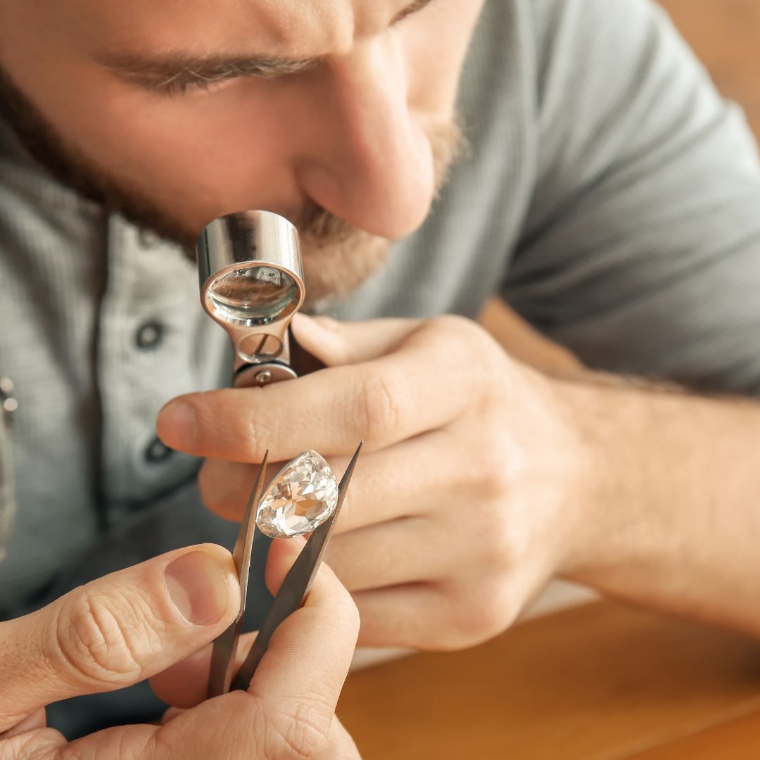 A jeweler is carefully inspecting a diamond using a loupe, gently securing it with tweezers for a Same Day Jewelry Appraisal. Certified assessments are offered immediately, guaranteeing both quality and convenience.