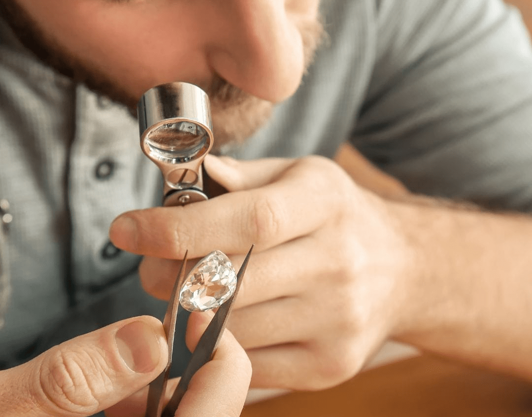 Jeweler examining a large pear-shaped gemstone with tweezers under a magnifying loupe, highlighting detailed appraisal work.
