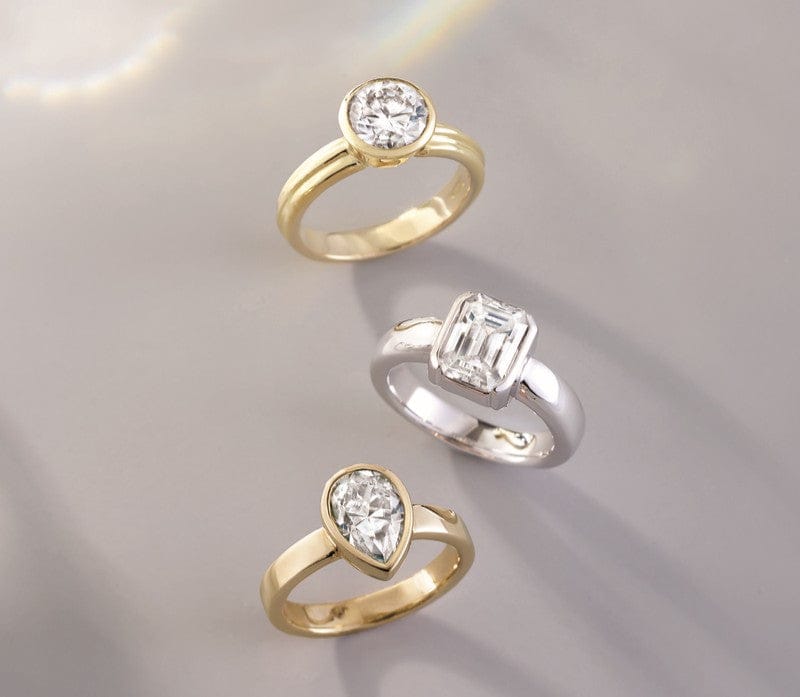 Three diamond bezel set rings in gold and white gold on a soft gray background