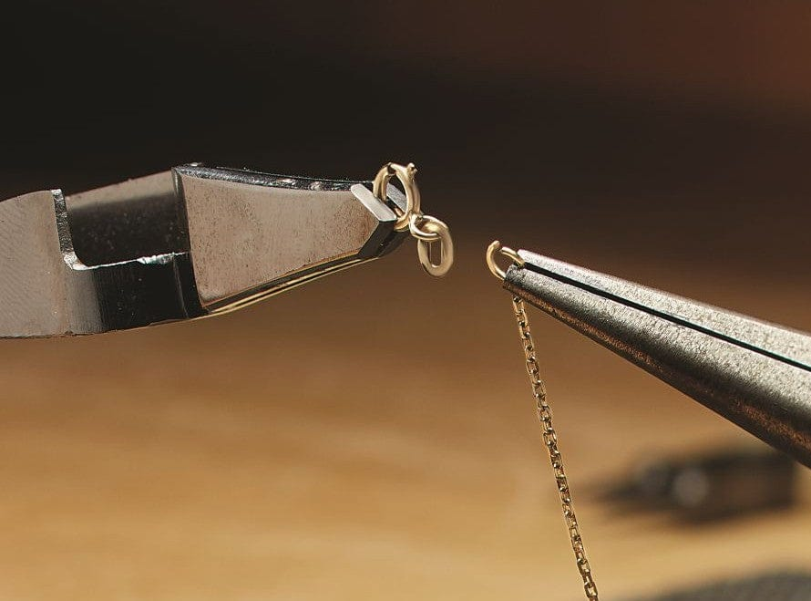 Close-up of jewelry-making chain repair with pliers and gold chain on a dark background
