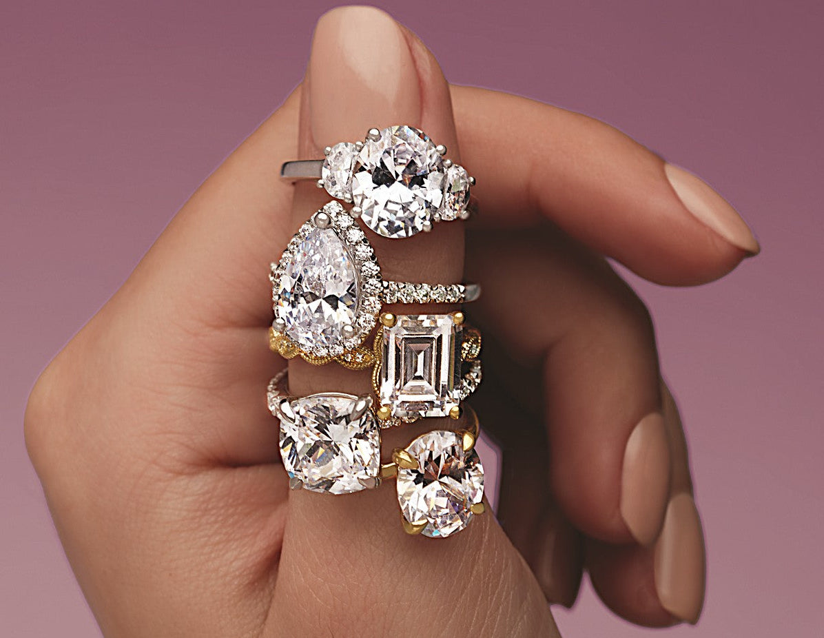 Close-up of a hand displaying six diamond engagement rings in various cuts and settings, showcasing custom jewelry design expertise.