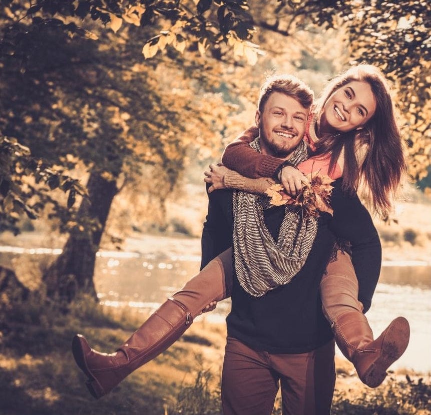 Man getting engaged to a woman in a park with trees and water in the background