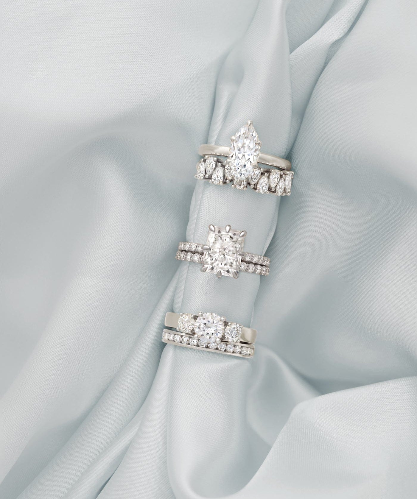 Three diamond engagement rings with bands, displayed on light blue satin fabric.