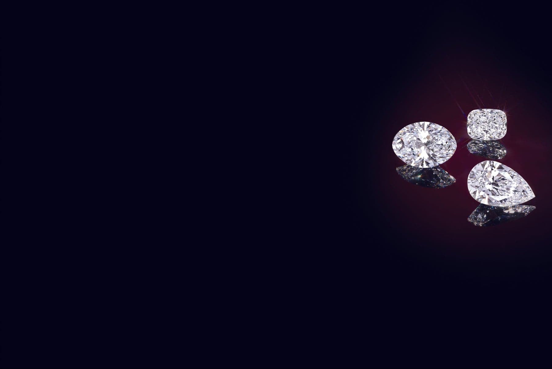 Three lab grown diamonds of different shapes on a dark background