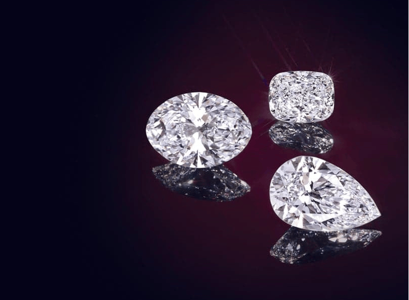 Four lab grown diamonds of different shapes on a reflective dark surface