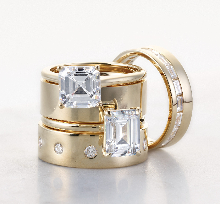 Two gold rings with emerald-cut diamonds on a light background