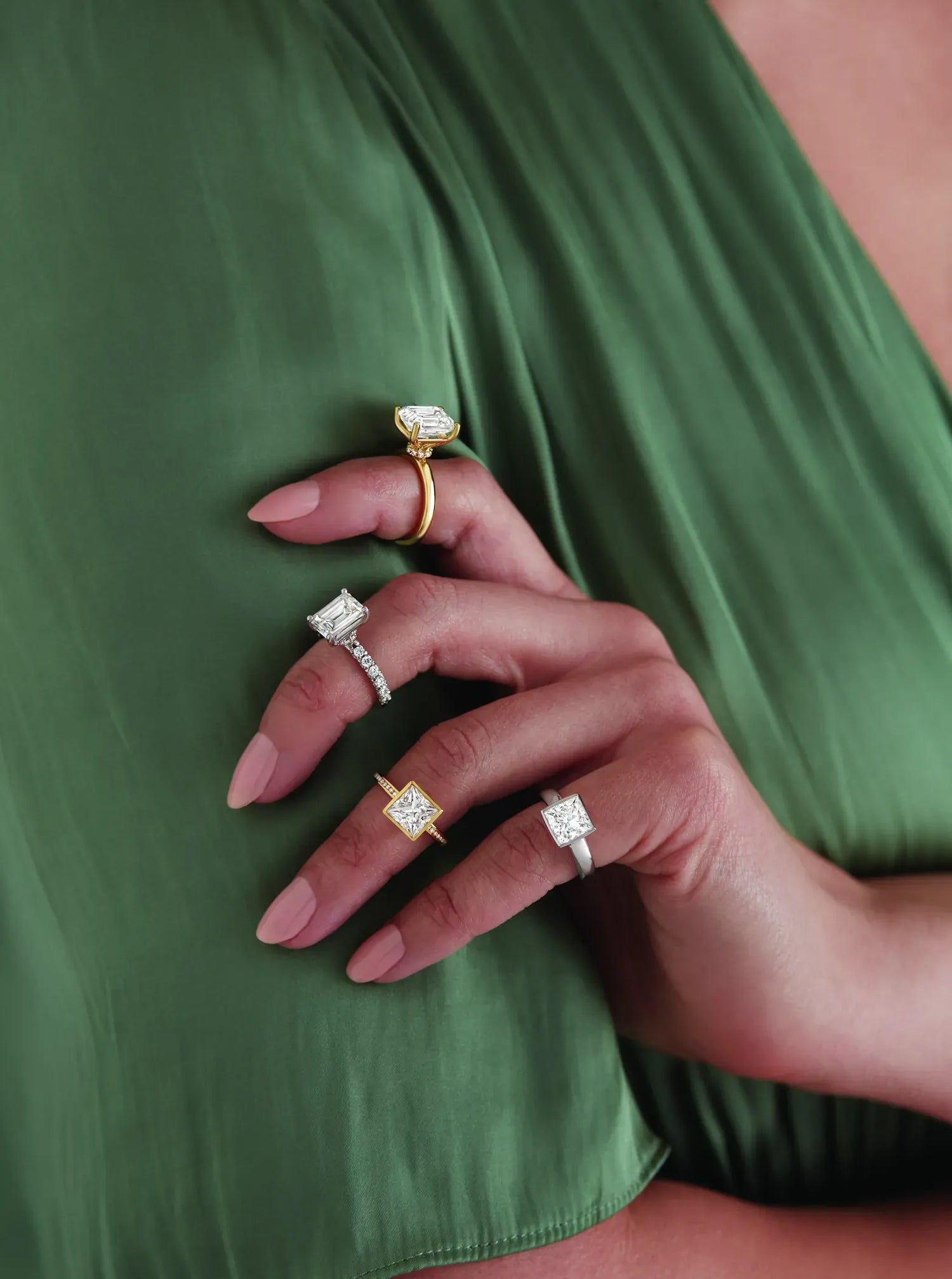 Close-up of a hand wearing multiple diamond rings on a green fabric background