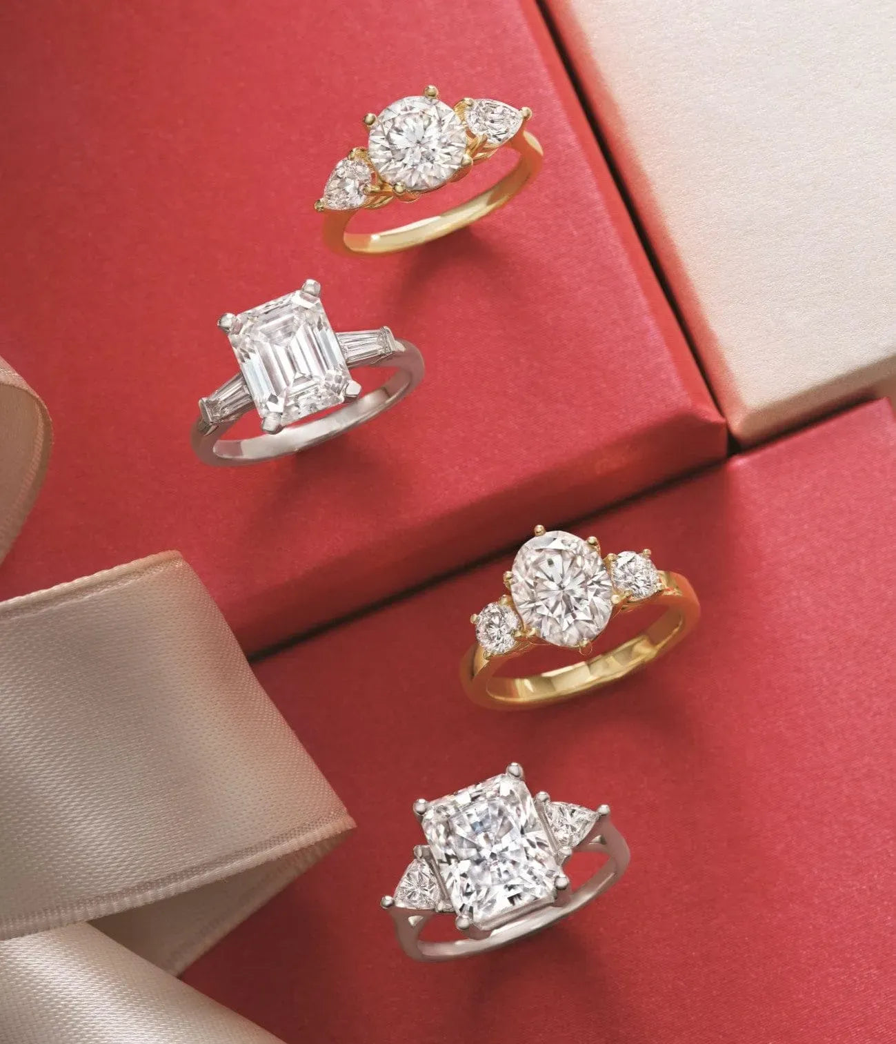 Four diamond engagement rings on a red surface with a beige ribbon.