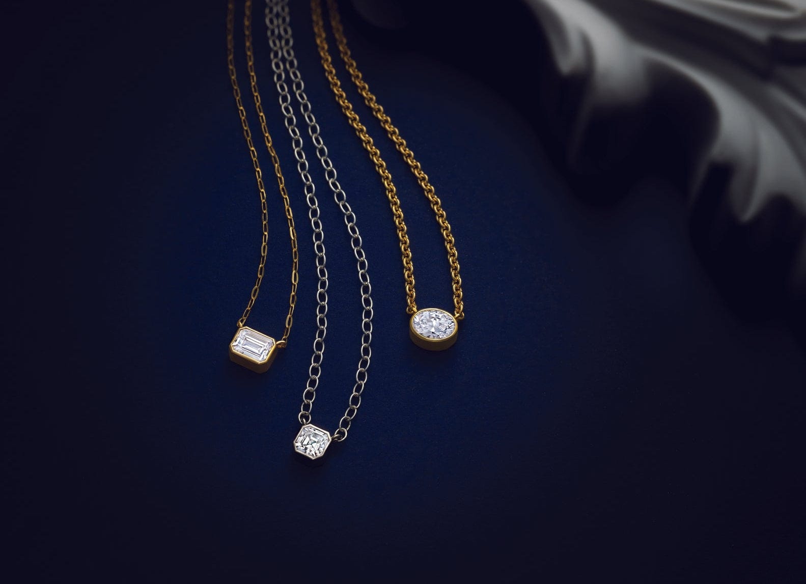 Three lab grown diamond necklaces on gold chains against a dark background