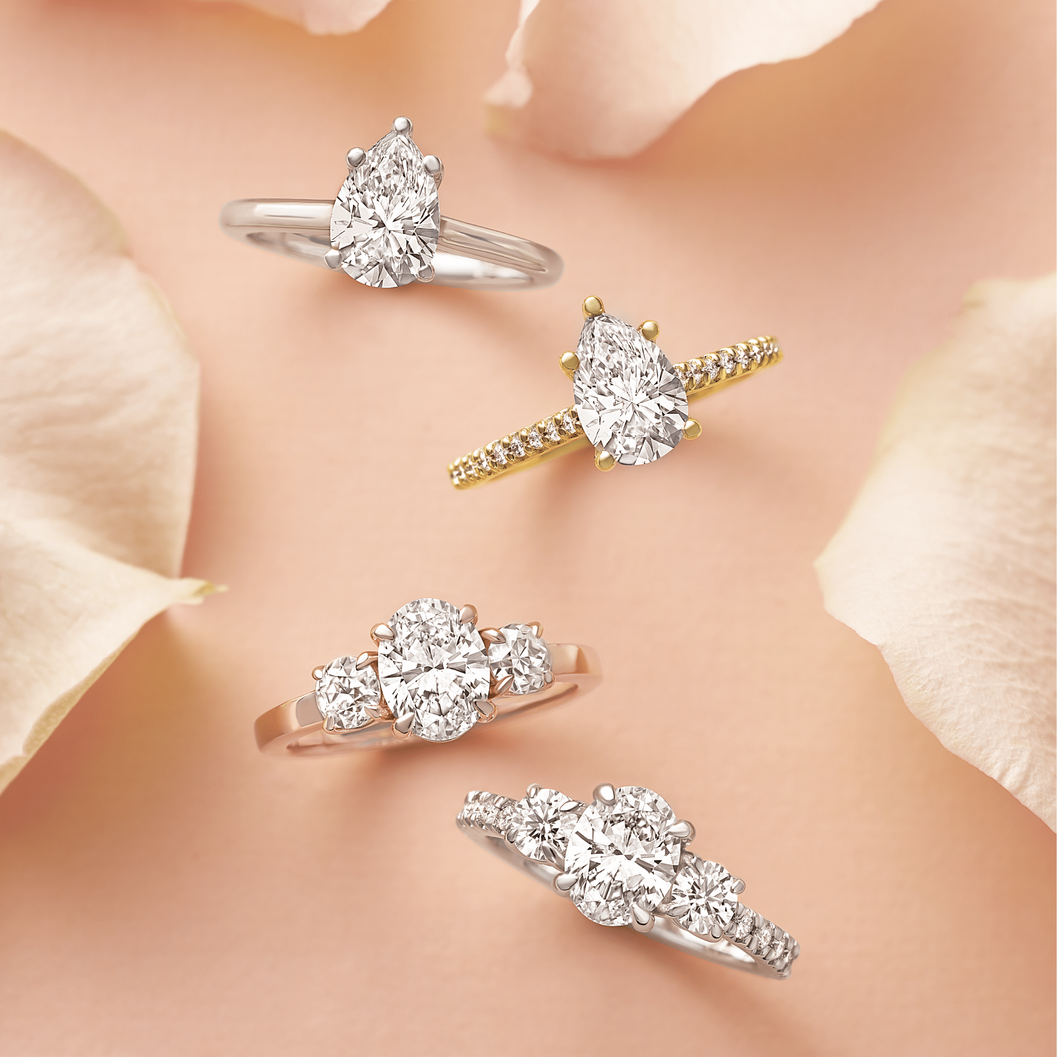 Four diamond engagement rings in gold and silver settings on a peach background with rose petals.