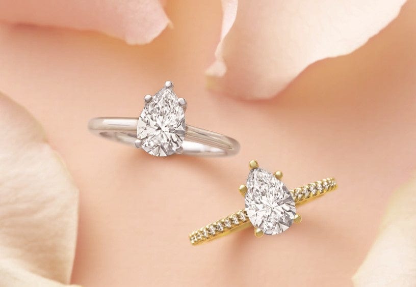 two pear shaped lab grown diamond engagement rings on a peach surface.