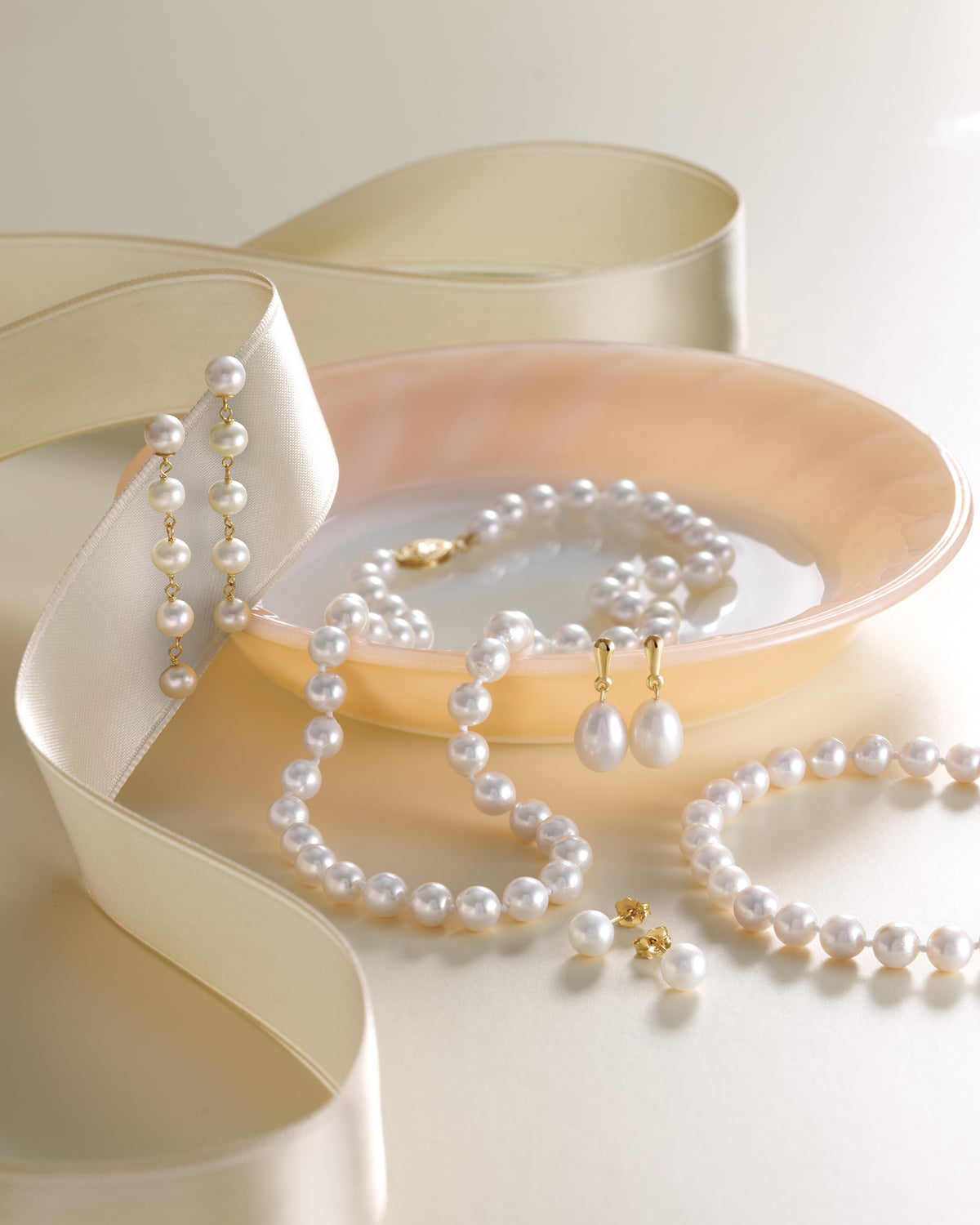 Pearl jewelry set including necklace, earrings, and bracelet on a white surface with a beige heart-shaped box.