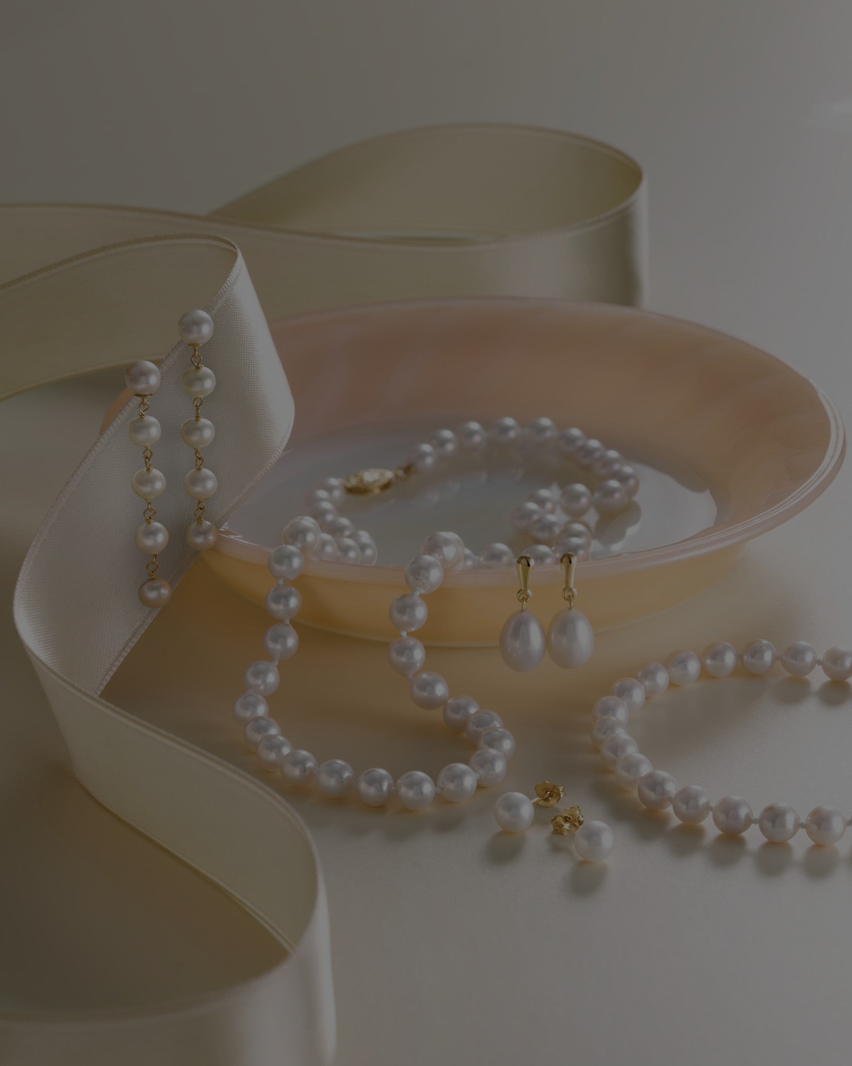 Pearl jewelry set including necklace, earrings, and bracelet on a white surface with a beige heart-shaped box.