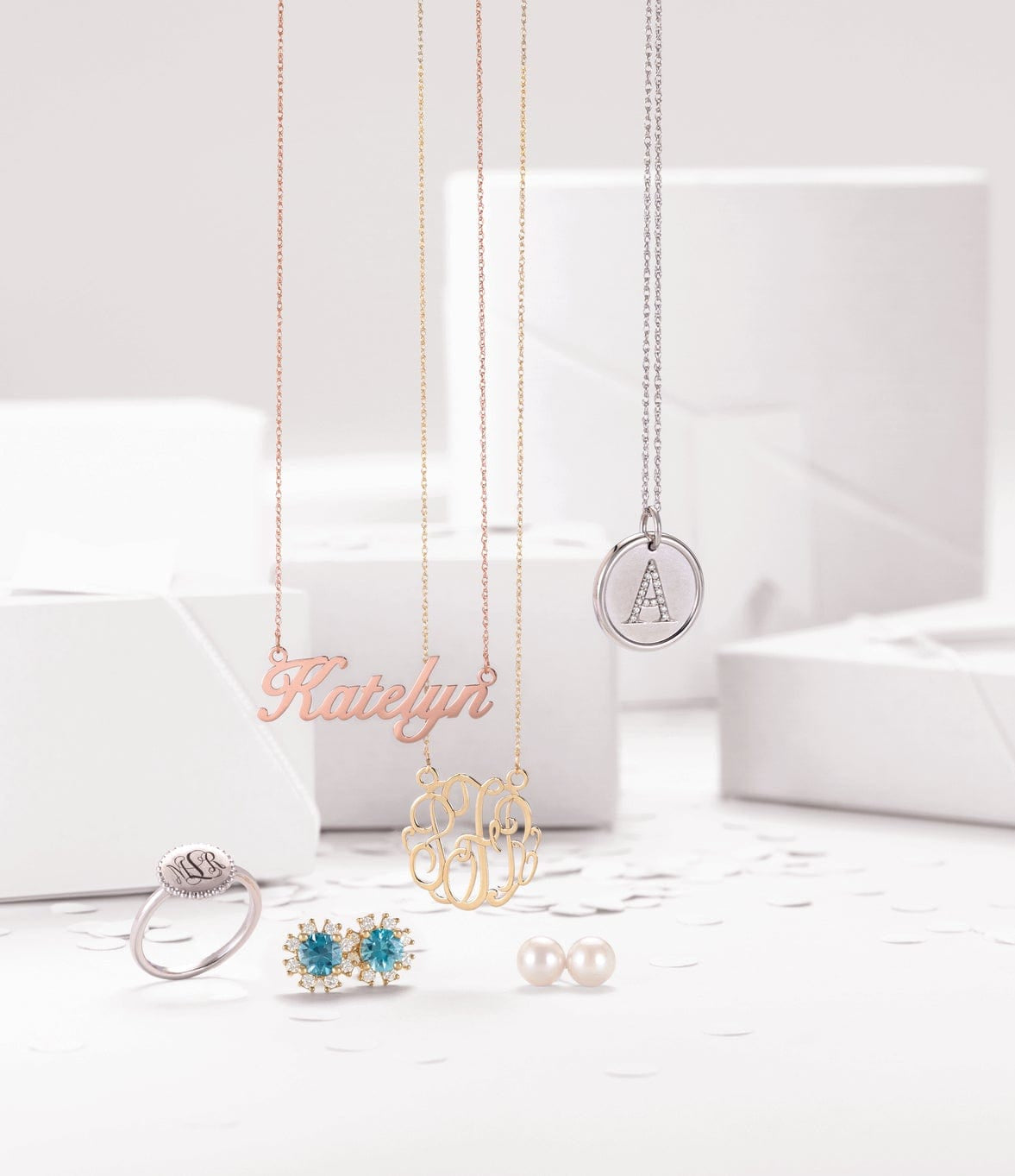 Assorted personalized necklaces, rings, and earrings displayed on white boxes with confetti on a white background.