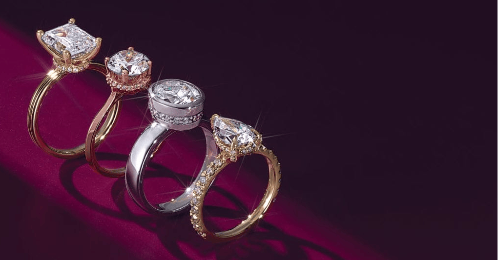 Four diamond rings, three gold and one silver, on a dark red background