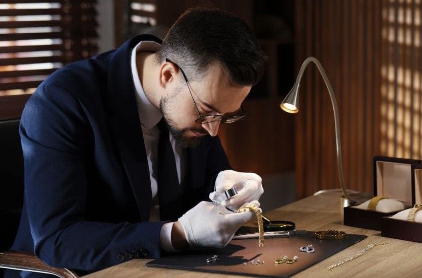 Graduate gemologit examining jewelry with a magnifying glass in a dimly lit roomist  