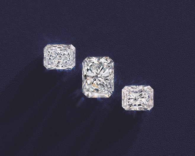 Three radiant-cut diamonds arranged in a row casting subtle shadows on a deep blue surface.