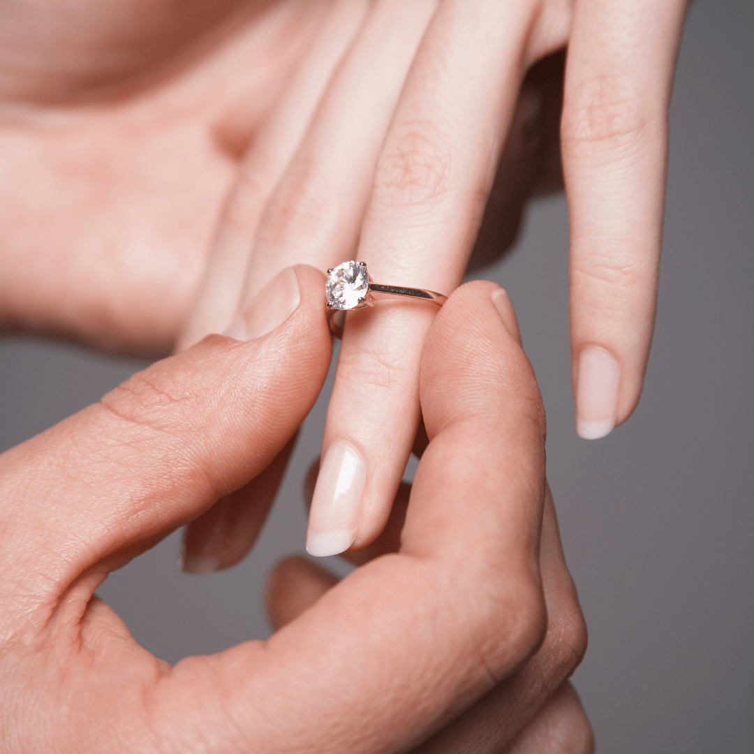 A hand placing a diamond engagement ring on another persons ring finger.