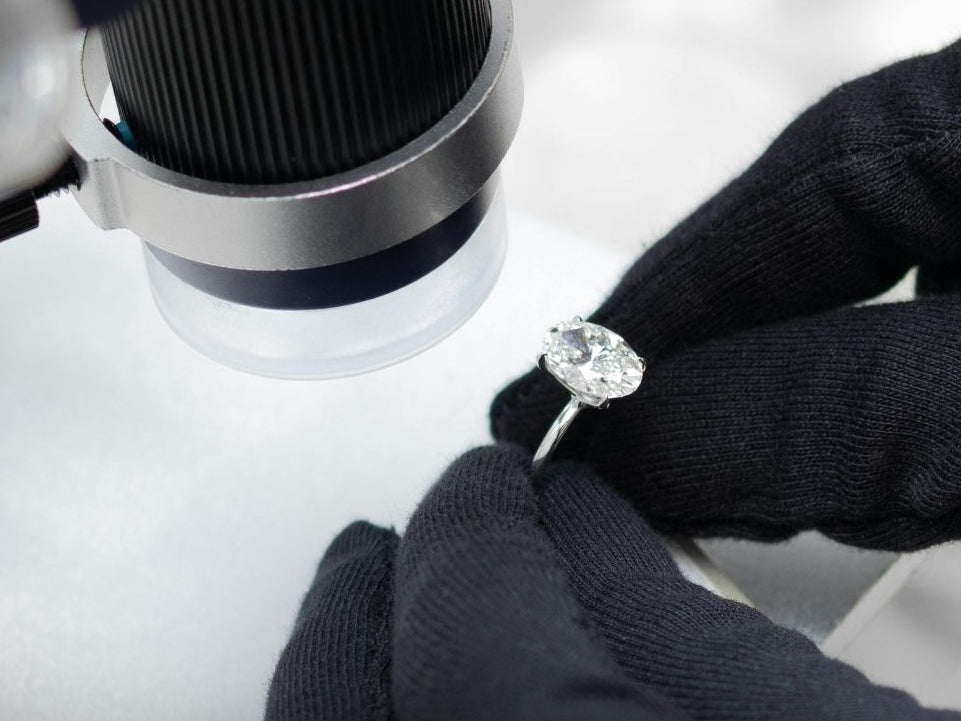 Person examining a diamond with a magnifying glass in a controlled setting