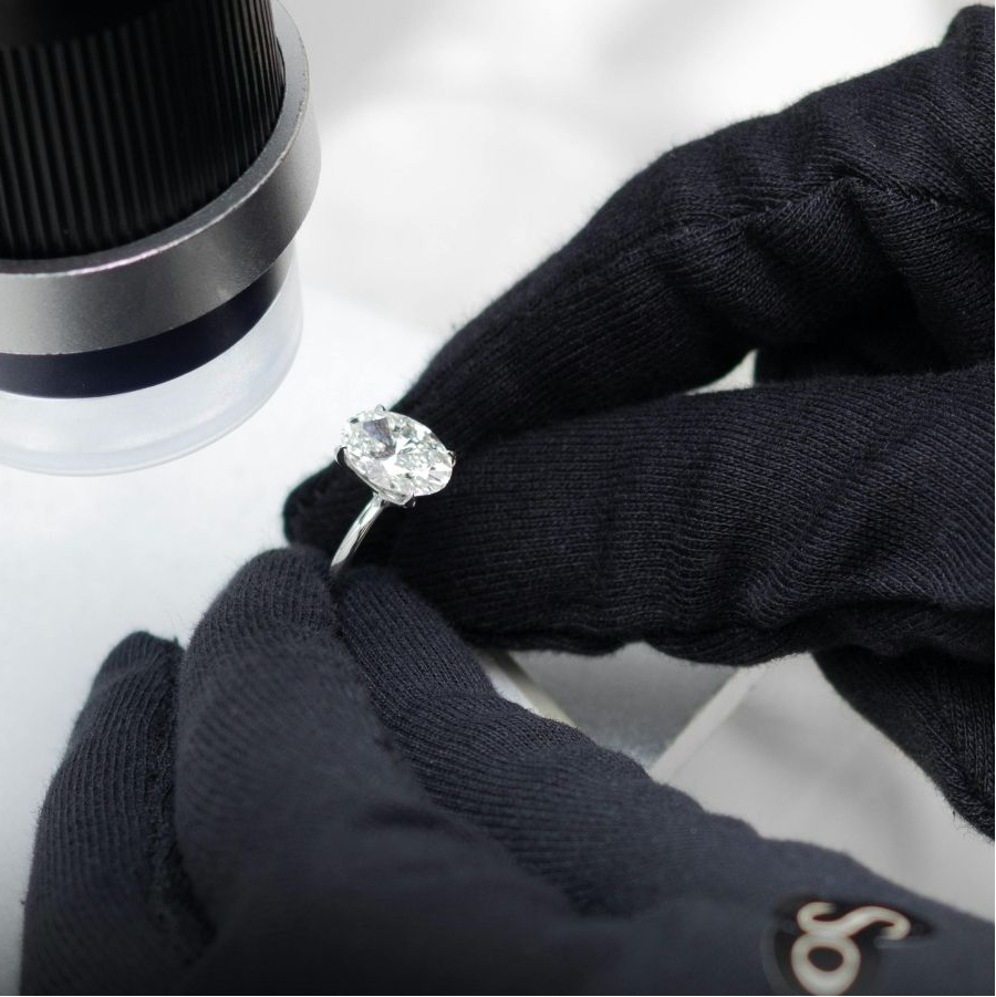 Diamond ring being examined under a magnifying glass by gloved hands.