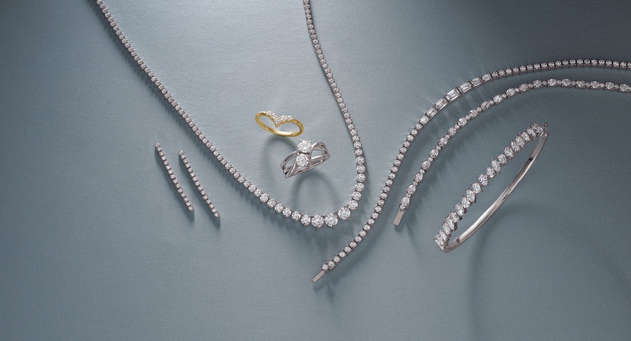 Jewelry set including a ring, bracelet, and diamond tennis necklace on a gray background