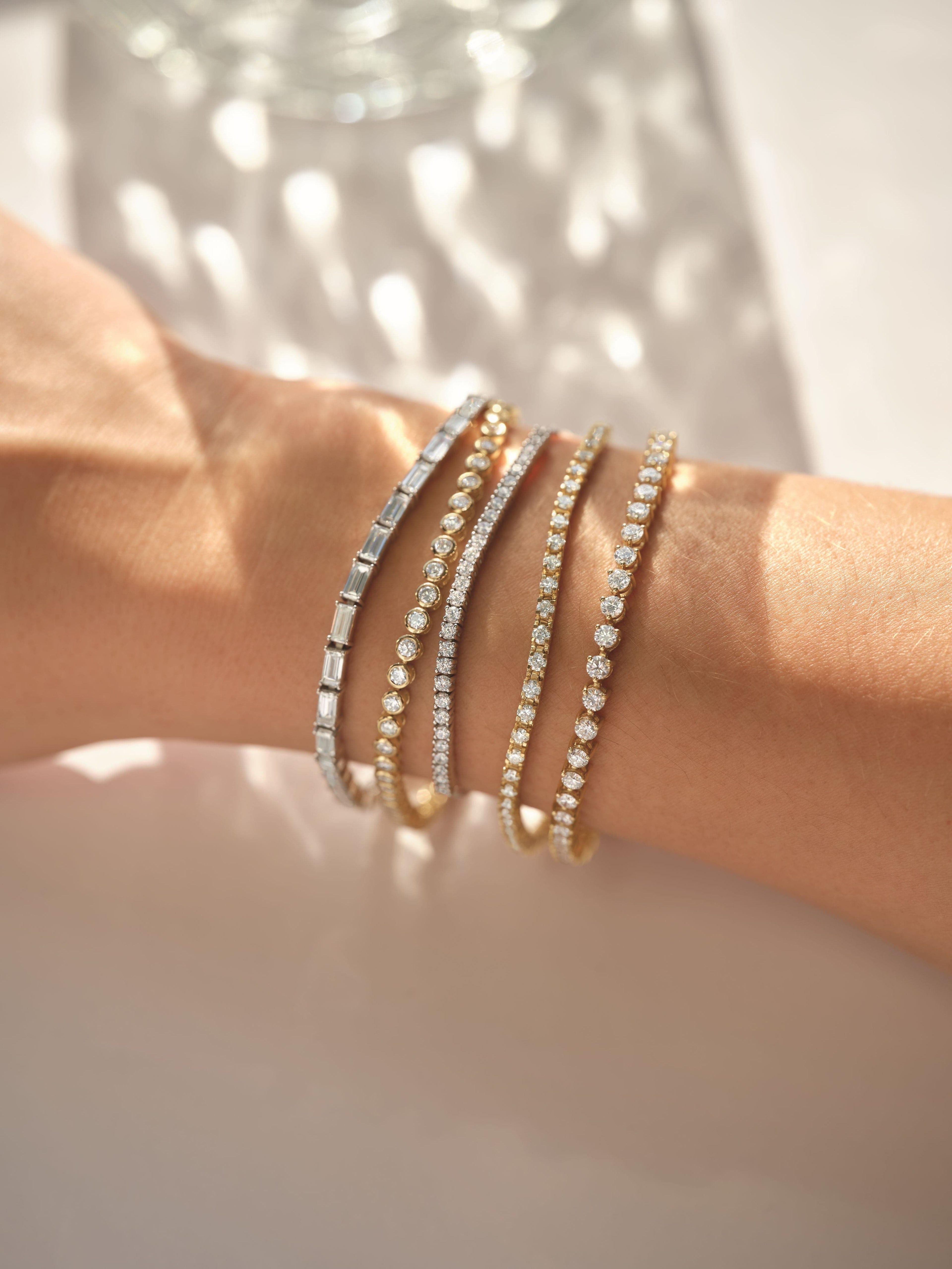 Close-up of a wrist wearing multiple diamond tennis bracelets with a soft background