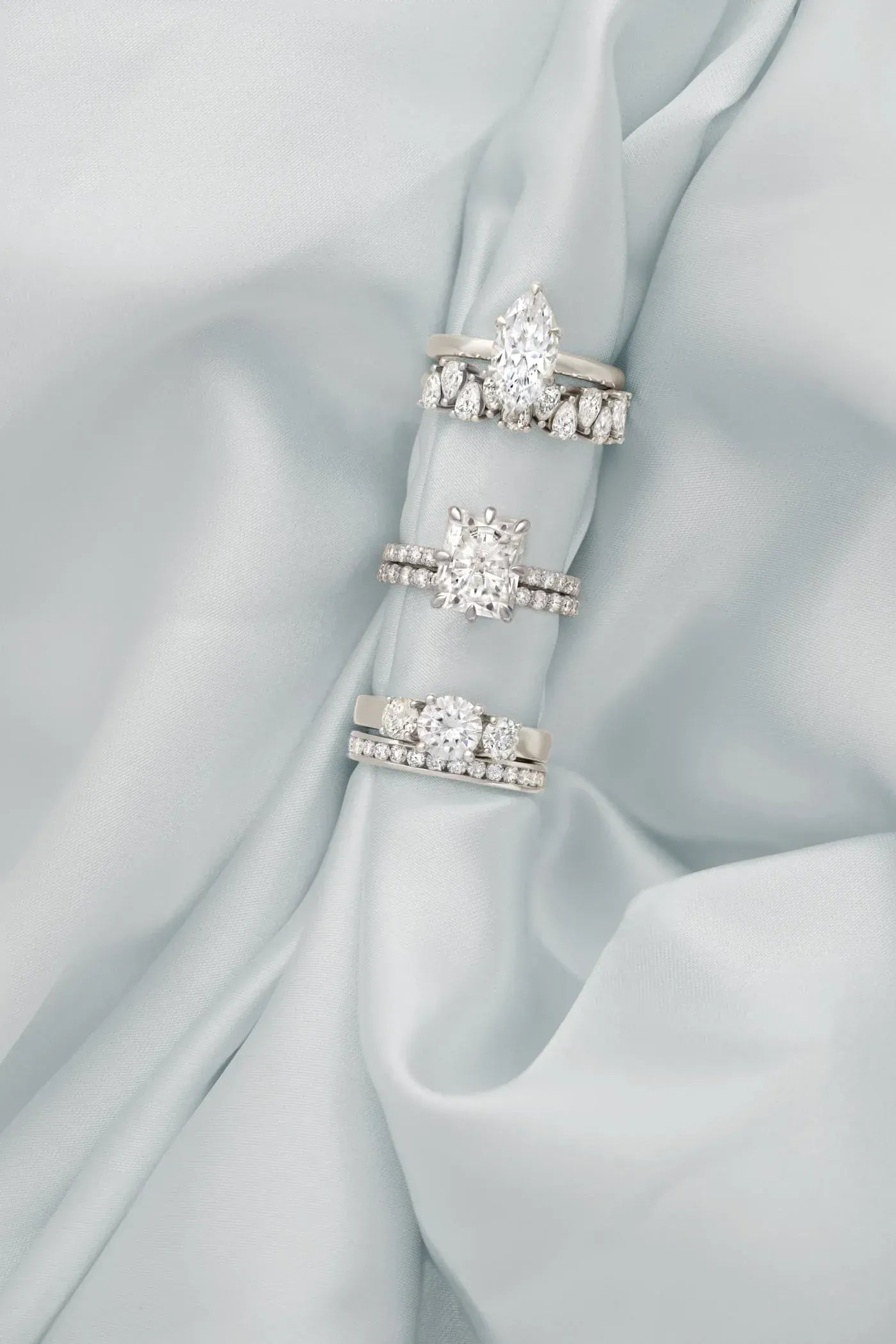 Three white gold engagement rings with gemstones on a light blue satin background