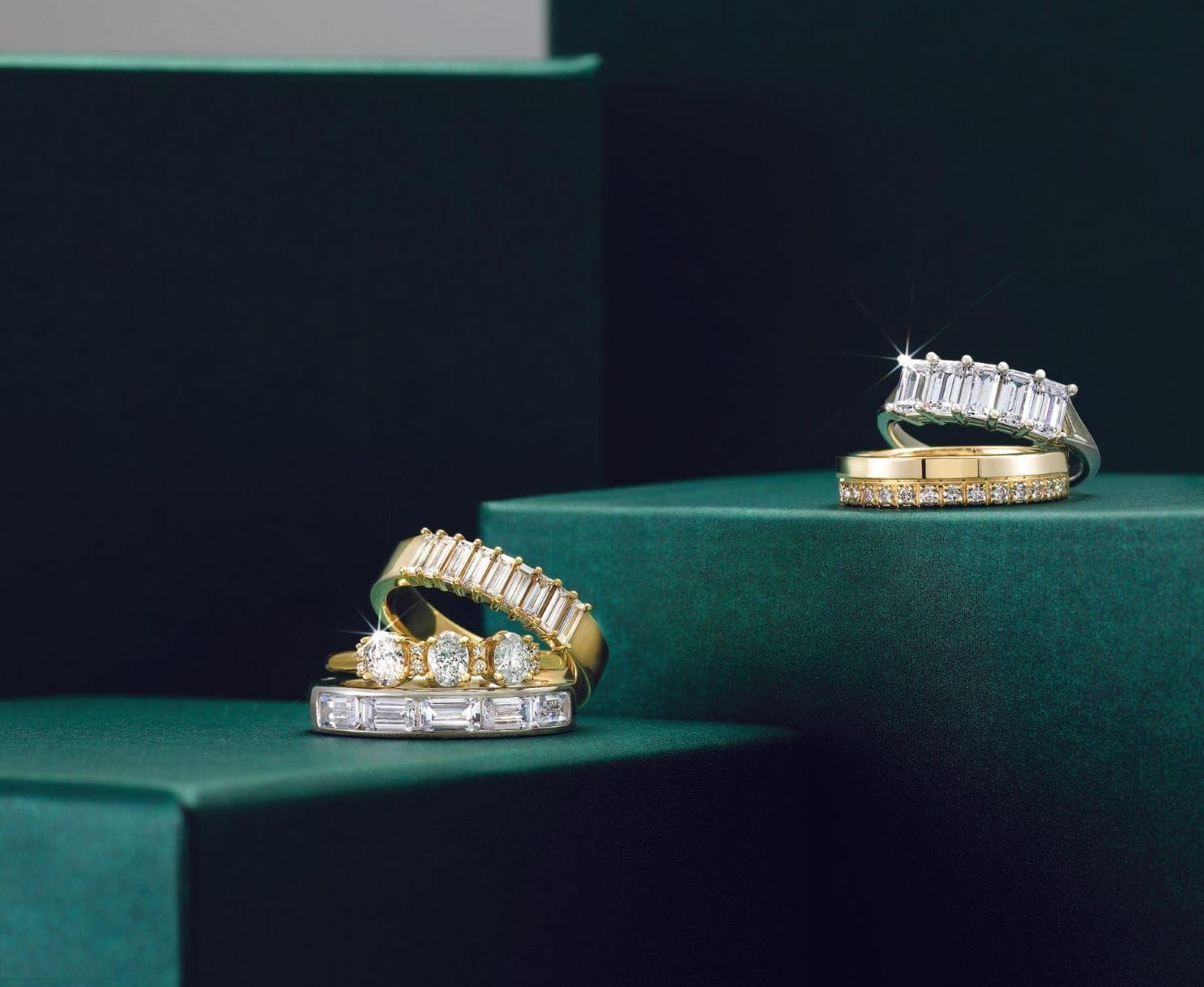gold and diamond wedding band stacks laying on a green surface.