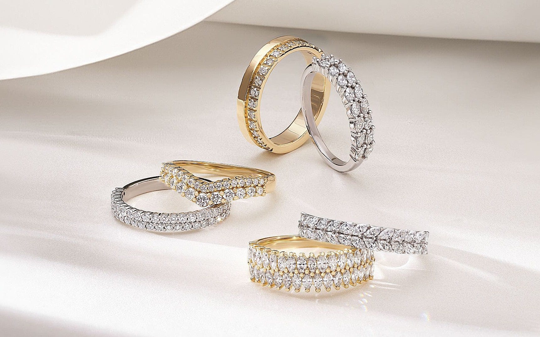 Five diamond-studded gold and silver rings are arranged on a smooth, light-colored surface.