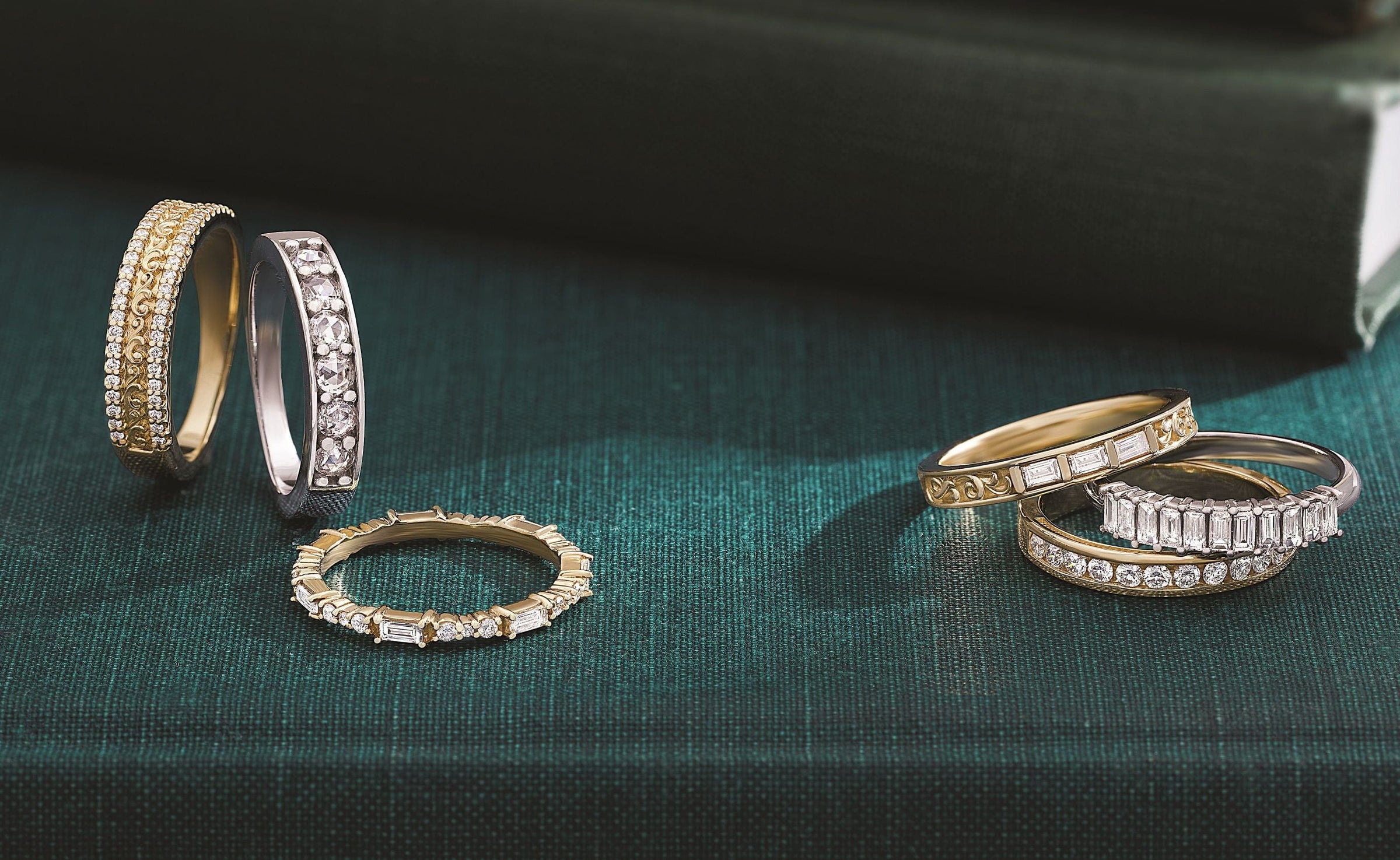 Six gold and silver diamond rings displayed on a dark green textured surface with books in the background.