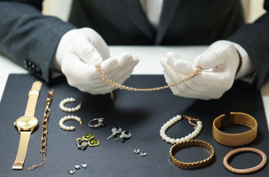 Person wearing white gloves handling gold jewelry on a dark surface